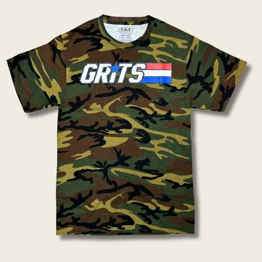 A short-sleeve crewneck t-shirt featuring a green, brown, and black camouflage pattern. The chest is printed with the word 'GRITS' in bold white letters, with a blue star replacing the 'I', and a small red, white, and blue flag graphic behind it.