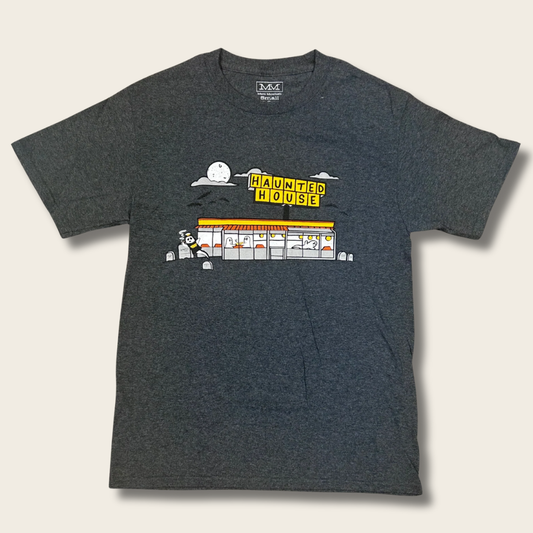 A dark heather gray t-shirt featuring a cartoon graphic of a haunted house with a yellow sign that reads 'HAUNTED HOUSE' and a ghost character, shown against a light beige background.