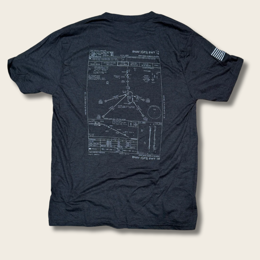 A dark navy blue t-shirt shown from the back, featuring a large white technical blueprint-style graphic of a Navy GCS Plan 1978 map on the back. A small white striped flag graphic is printed on the left sleeve.