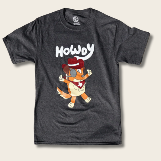 A dark heather gray t-shirt featuring a cartoon graphic of a dog dressed as a cowboy with the word 'HOWDY' printed above it, displayed on a light beige background.