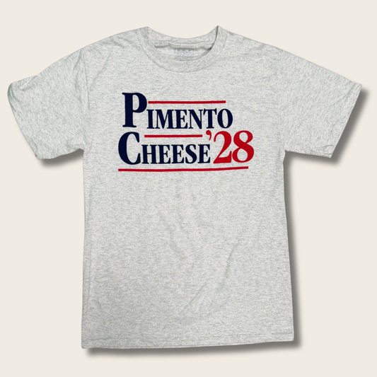 A light heather gray crewneck t-shirt featuring a 'PIMENTO CHEESE '28' graphic on the chest in navy blue and red, displayed against a light beige background.